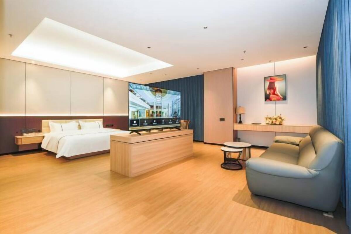 A modern hotel room with a bed, a seating area, a TV, and a desk.
