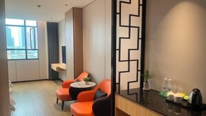 A hotel room with a modern design, featuring a large window with a city view, two orange chairs, a small round table, and a black and white geometric wall decoration. - Jewel Business Hotel (Kaiping)
