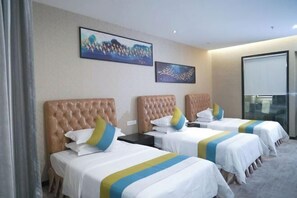 A hotel room with three beds, each with a tufted headboard and white bedding with blue and yellow accents. There are two framed artworks on the wall above the beds. - Jewel Business Hotel (Kaiping)