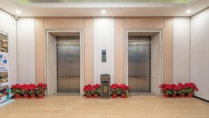 A modern elevator area with two elevators, a small trash bin, and red potted plants. - Jewel Business Hotel (Kaiping)
