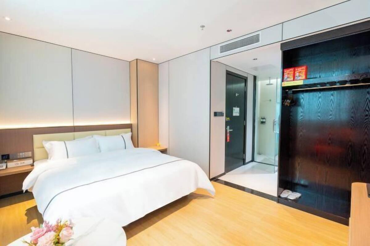 A modern hotel room with a large bed, a wardrobe with a mirror, and a small bedside table.
