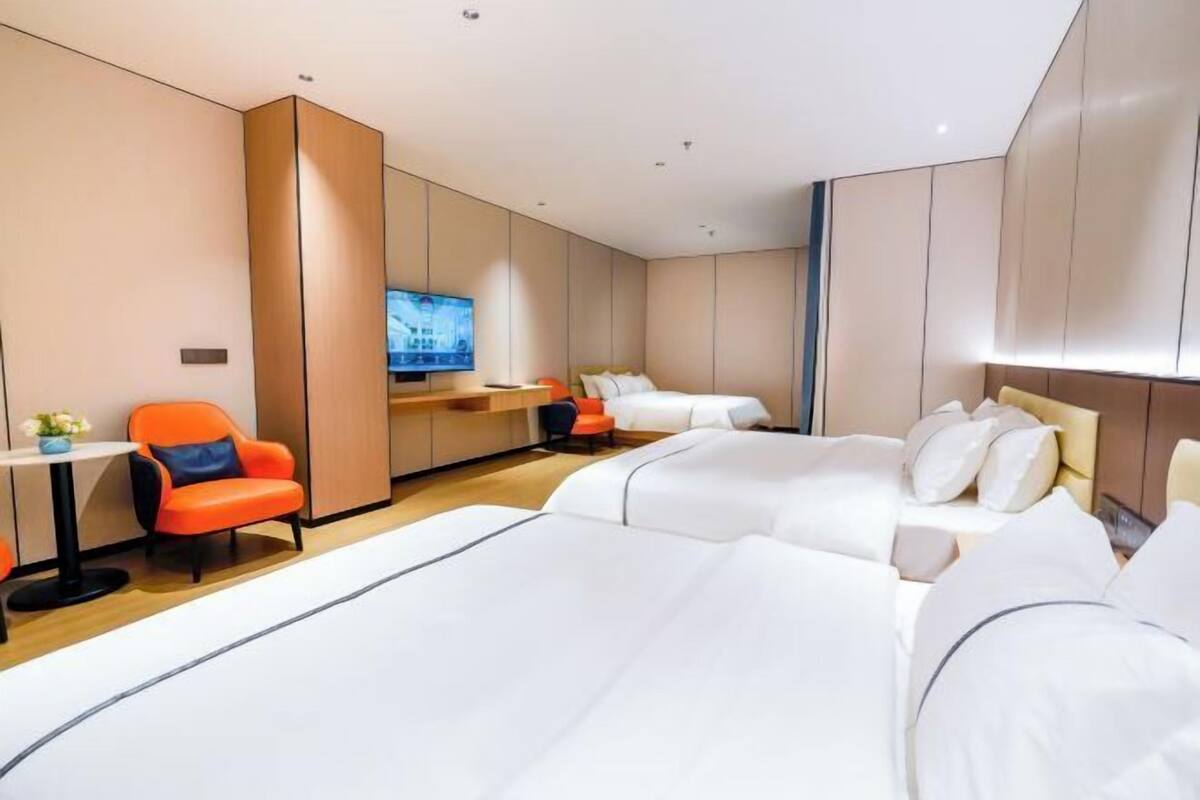 A hotel room with two beds, a desk, a TV, and a seating area.