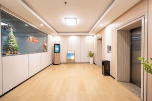 Vestíbulo de hotel con piso de madera, mostrador de recepción, quiosco digital, un árbol de Navidad y un ascensor.