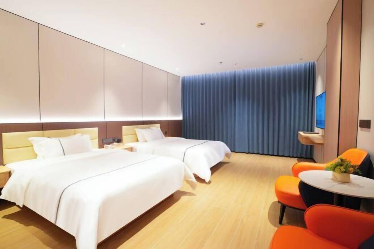 A hotel room with two beds, a small table with a plant, and orange chairs.
