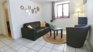 A living room with a black sofa, a round coffee table, and a dark armchair. There is a lamp on a side table, and a window with curtains. - L'Alsacienne - cosy gite (Eguisheim)