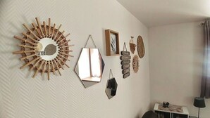 A room with a white textured wall, a round mirror, a hexagonal mirror, and a small table with a lamp. - L'Alsacienne - cosy gite (Eguisheim)