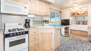 Eine kompakte Küche mit Herd, Mikrowelle und Kaffeemaschine. Es gibt eine kleine Essecke mit Tisch und Stühlen sowie ein Schlafzimmer mit Bett und Fernseher.