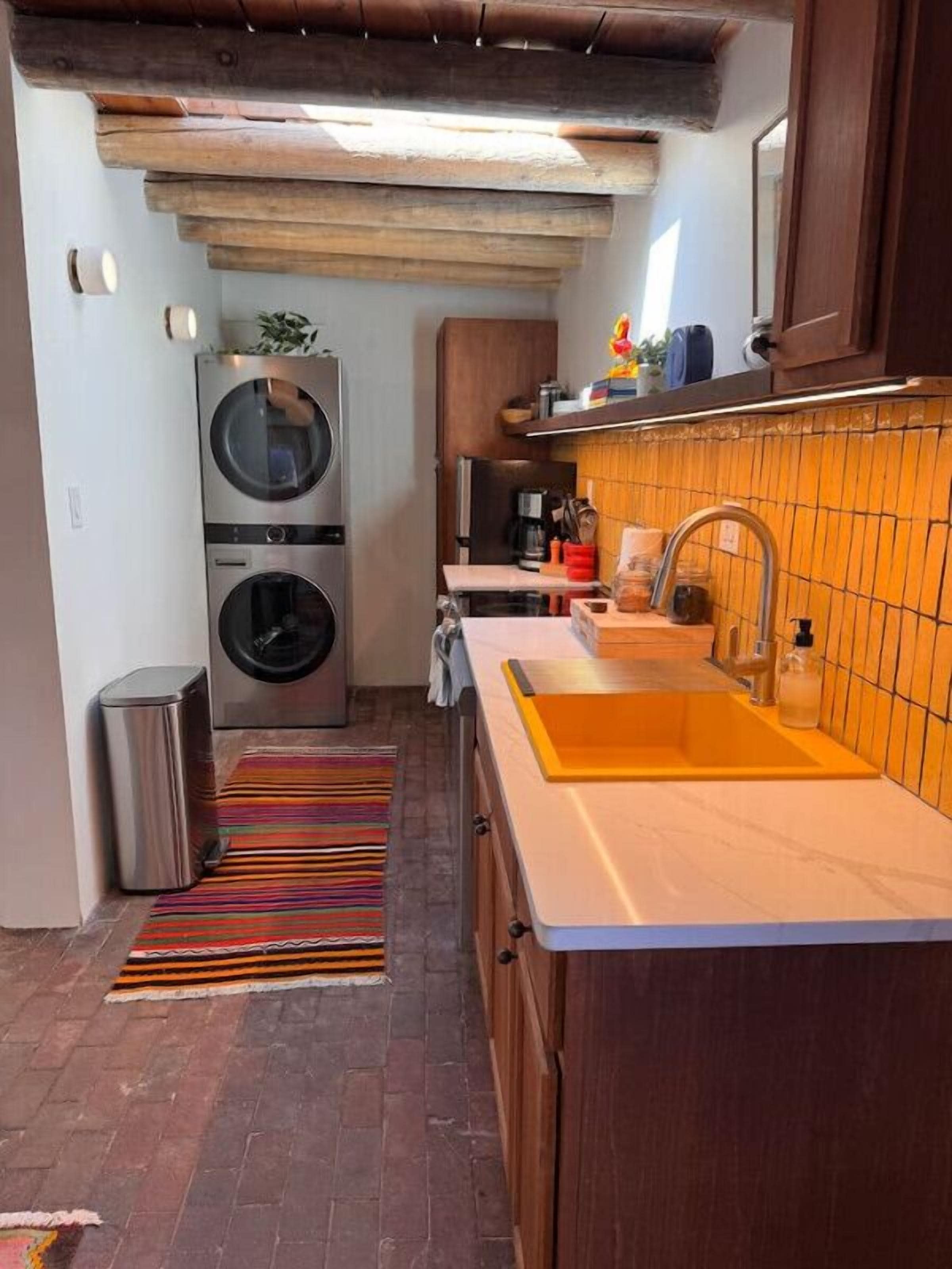 A compact kitchen with a built-in washer and dryer, a sink with a yellow backsplash, and a striped rug on the floor.