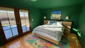 Un dormitorio con una cama grande, un tapete colorido, un cuadro en la pared y vistas a través de la puerta corrediza de vidrio.