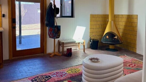 Una habitación acogedora con techo de madera, chimenea, alfombra colorida y una pequeña mesa con una caja.