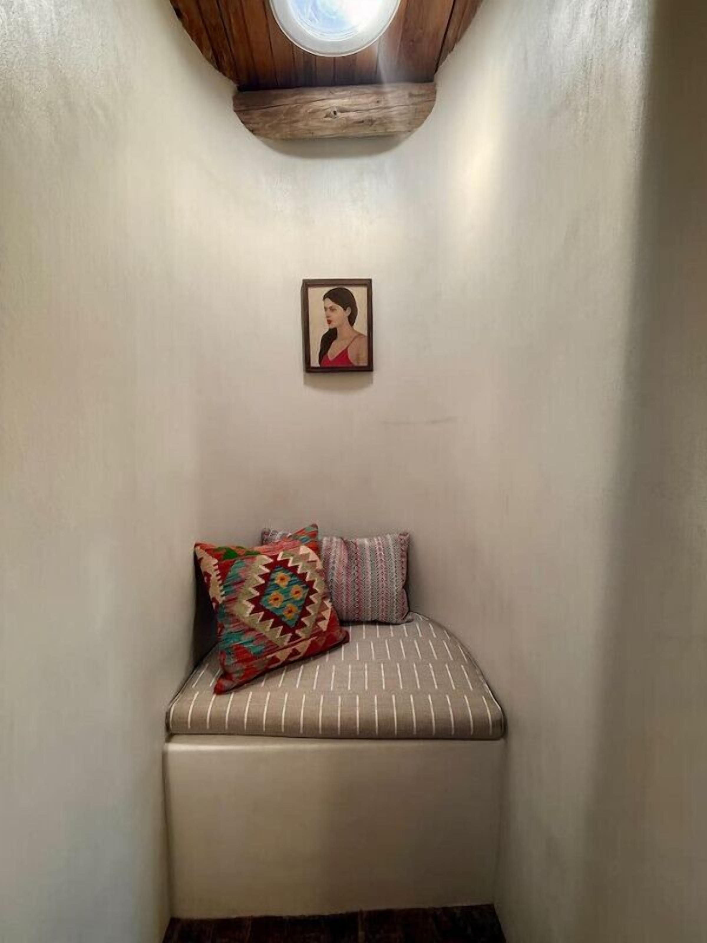 Una habitación pequeña y acogedora con un banco, dos almohadas y un cuadro en la pared.