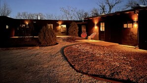 Un edificio con camino de grava, una silla roja y fachada bien iluminada al anochecer.