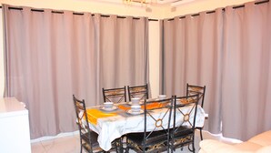 A dining area with a table set for six, surrounded by chairs, curtains, and a chandelier. - Manacomfy - 14bed House - 4 Baths - Victoria Falls (Victoria Falls)