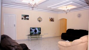 A living room with a television, a sofa, and a black armchair. - Manacomfy - 14bed House - 4 Baths - Victoria Falls (Victoria Falls)