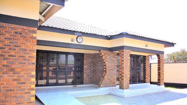 A two-story building with a tiled roof, numbered 8509, featuring large glass doors and brick pillars. - Manacomfy - 14bed House - 4 Baths - Victoria Falls (Victoria Falls)