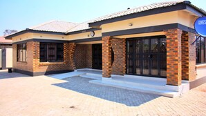 A two-story building with a tiled roof, brick columns, and large windows. - Manacomfy - 14bed House - 4 Baths - Victoria Falls (Victoria Falls)