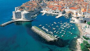 An aerial view of a historic coastal city with a fortified castle, clear blue waters, and numerous boats docked at the harbor. - Modern vacation apartment with pool and sea view (Pisak)