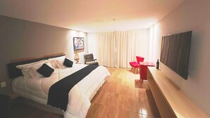 Una habitación de hotel moderna con una cama grande, un escritorio, una silla y un televisor en la pared.