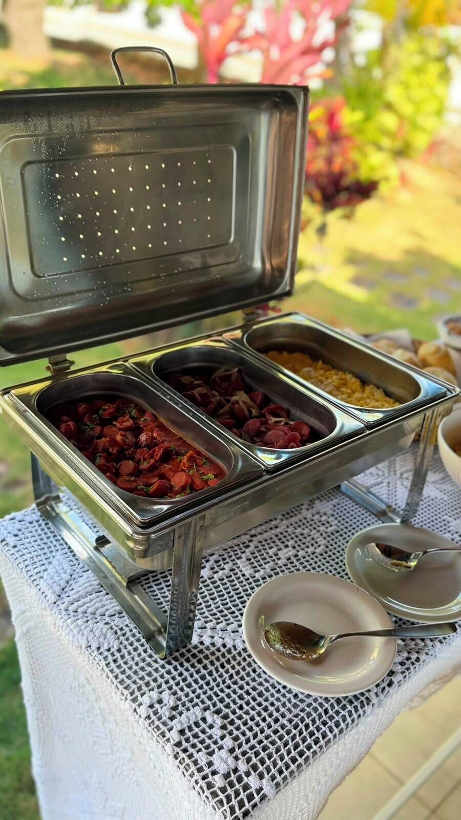 A buffet table with multiple food containers, a small bowl with a spoon, and a white tablecloth.