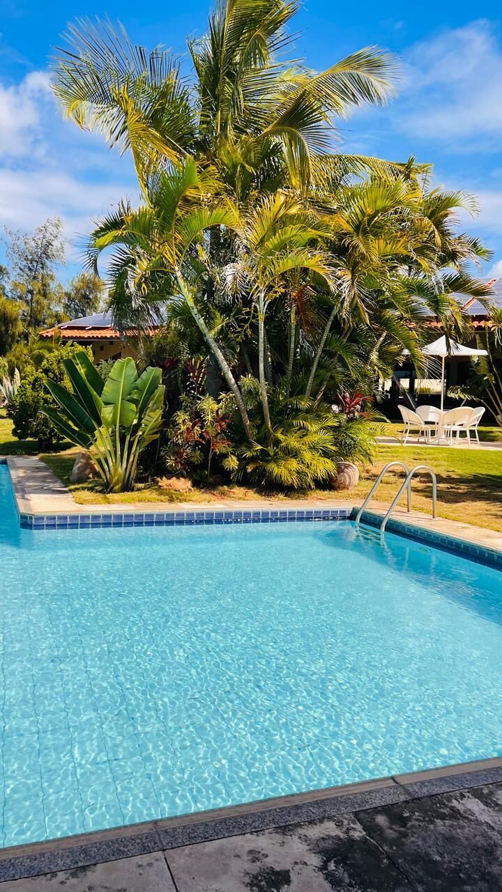 Una piscina azul cristalina rodeada de exuberante vegetación y un área de estar exterior con mobiliario blanco.