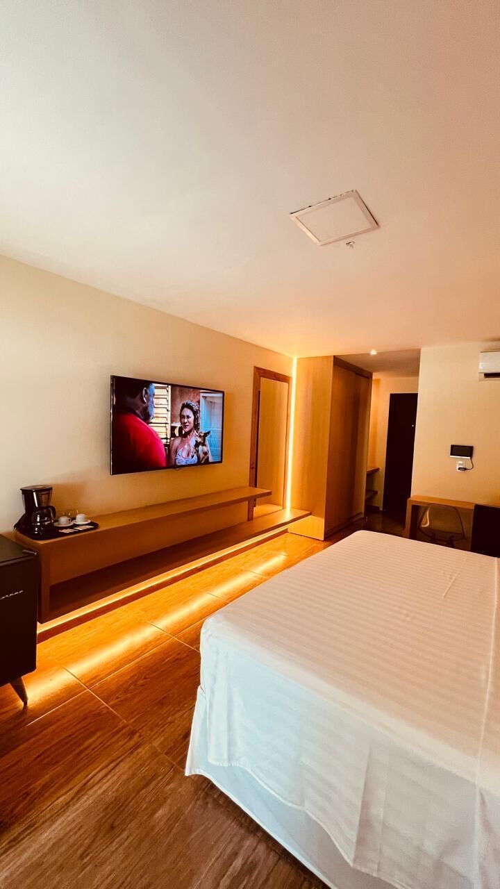 A hotel room with a bed, a TV mounted on the wall, a wooden bench, and a coffee maker.