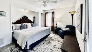 A bedroom with a bed, a ceiling fan, a desk, a chair, a lamp, and a window with curtains. - Hideaway Haven @ Lake Granbury (Granbury)