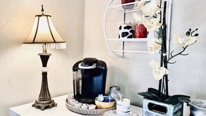 A coffee maker, a lamp, a tray with coffee pods, a plate with a mug, and a shelf with decorative items. - Hideaway Haven @ Lake Granbury (Granbury)