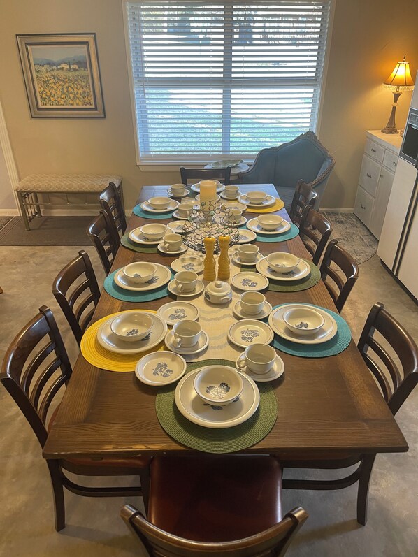 A dining table set for eight with a candle centerpiece, surrounded by chairs.