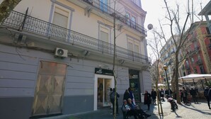 Un edificio con escaparate que dice “elle MIGUCCI” y un balcón con barandilla de metal.