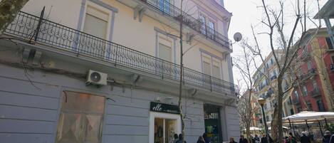 A building with a storefront labeled "elle MIGUCCI" and a balcony with a metal railing.