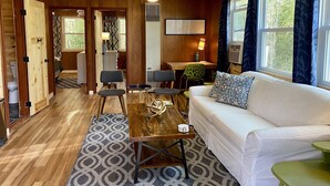 A cozy cabin interior with a wooden floor, a white sofa, a dining table, and a ceiling fan. - Fisherwaters Resort (Camdenton)