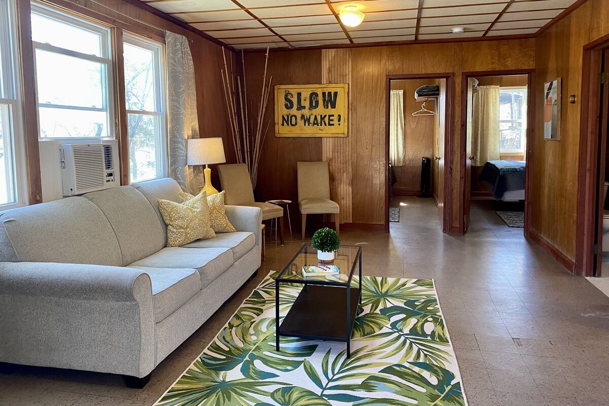 Uma sala de estar aconchegante com um sofá, uma mesa de centro e um aviso que diz "SLOW NO WAKE!".