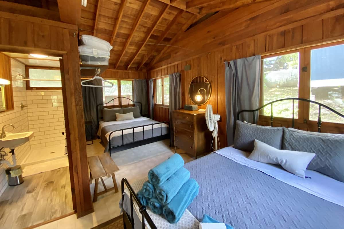 Quarto de cabana de madeira com cama, mesa de cabeceira, cômoda e janela com cortinas.
