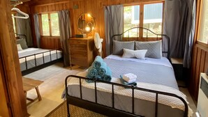 A wooden cabin bedroom with a bunk bed, a bedside table, a dresser, and a window with curtains. - Fisherwaters Resort (Camdenton)