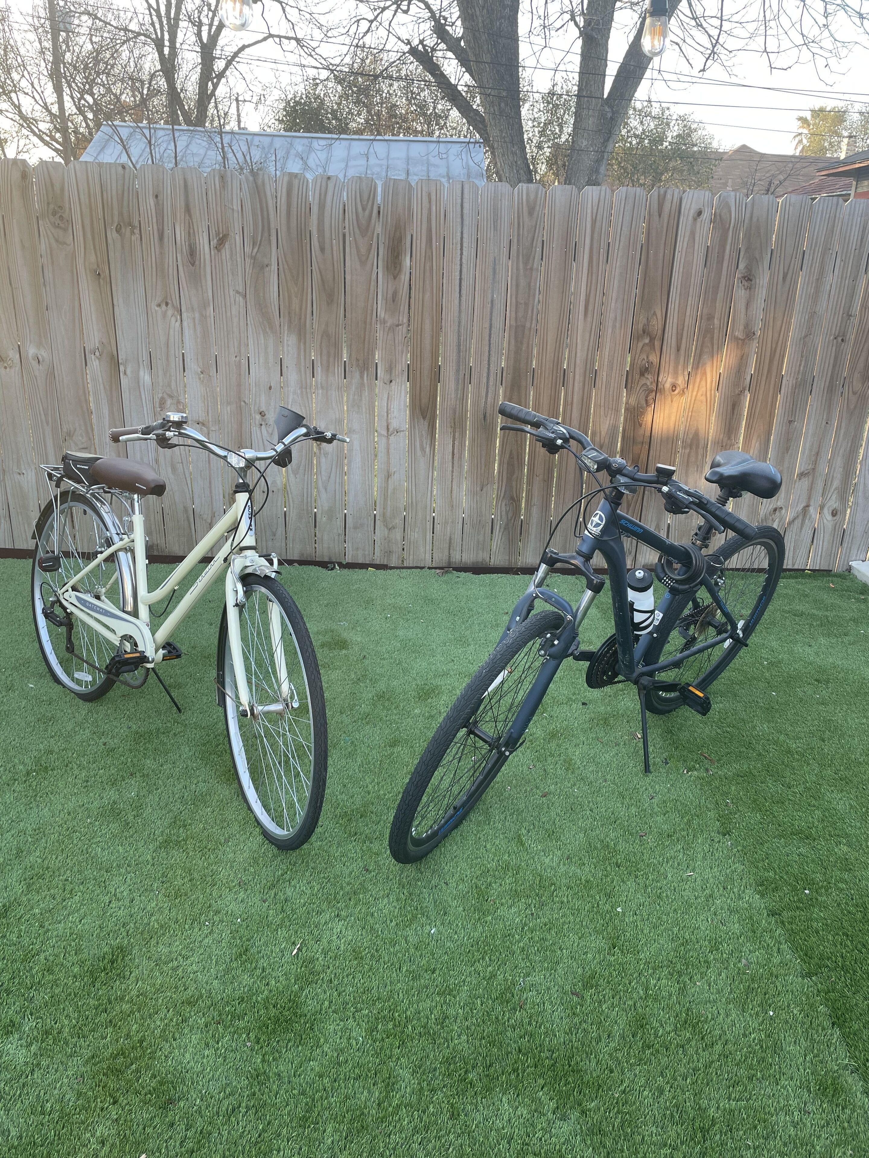 Dos bicicletas aparcadas sobre un césped con una valla de madera al fondo.