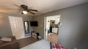 Una camera da letto con un letto, una ventola a soffitto, una televisione, un comò e una porta che dà su una cucina.