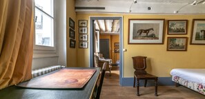 Una habitación con una cama, una mesa y una silla. Hay cuadros en la pared.