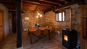 Un comedor rústico con pared de piedra, techo de madera y estufa de leña negra.