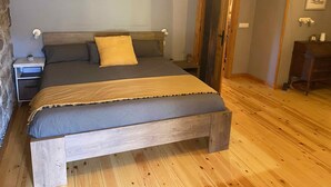 Un dormitorio con un cabecero de madera, un colchón gris y una mesita de noche de madera con una planta pequeña.