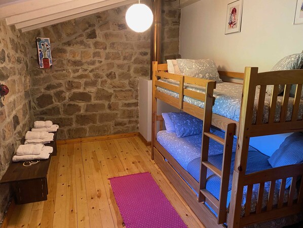 A cozy room with a bunk bed, a stone wall, and a wooden floor.