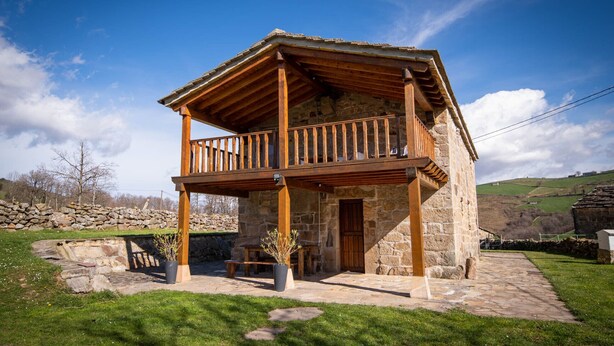 Una casa de piedra con un balcón de madera, un muro de piedra y un patio cubierto de césped.