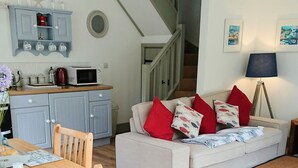 Ein modernes Wohnzimmer mit Sofa, Esstisch und Stühlen, einer Küchenzeile mit Schränken und Geräten sowie einer Treppe, die zu einer weiteren Ebene führt.