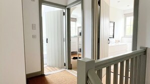 Ein Flur mit Teppichboden, einem Holnlaufgeländer und einer Tür zu einem Zimmer mit Fenster.