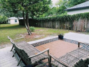 Relax in the serene backyard patio area with a comfortable seating area featuring two wicker chairs and a small table.