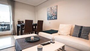 A modern living room with a white sofa, a coffee table, and a dining area with chairs and a table.