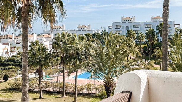A resort with a pool, palm trees, and white buildings in the background.
