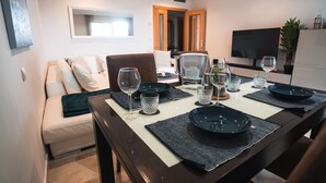 A dining area with a table set for four, a sofa, a TV, and a door leading to another room.