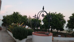 A paved outdoor area with a circular planter, a metal lamp post, and surrounding greenery. - Pias Guesthouse (Serpa)