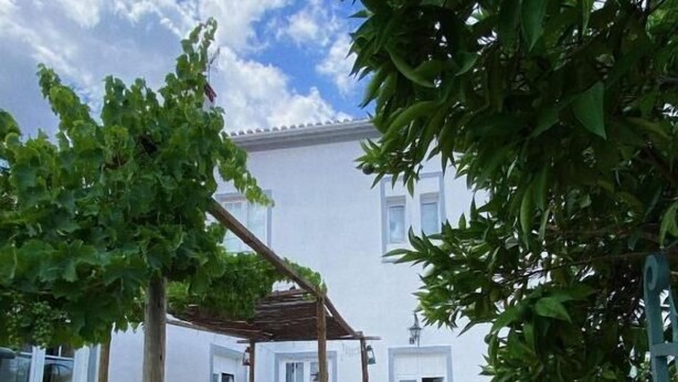 A courtyard with a pergola, a table with chairs, and a building with white walls and windows. - Pias Guesthouse (Serpa)