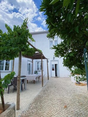 A courtyard with a pergola, a table with chairs, and a building with white walls and windows. - Pias Guesthouse (Serpa)